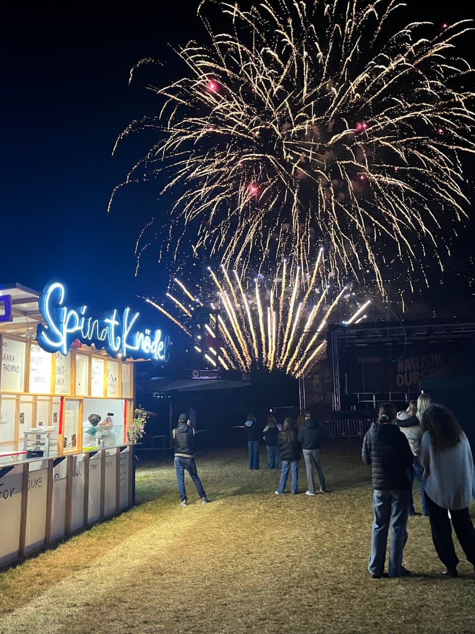 Spinat Knödel booth at night with fireworks in the background