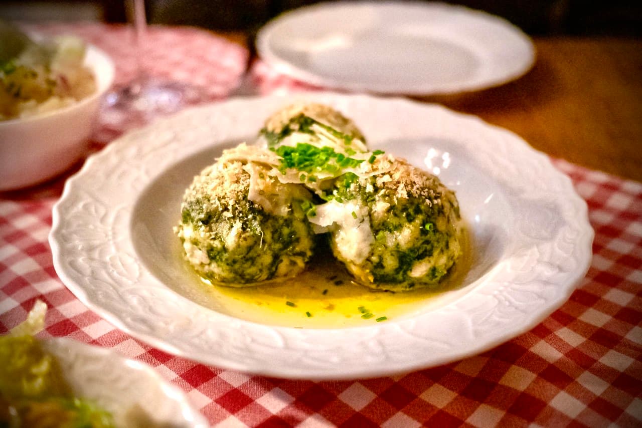 Spinach knödel on white plate with red checkered tablecloth, parmesan and chives